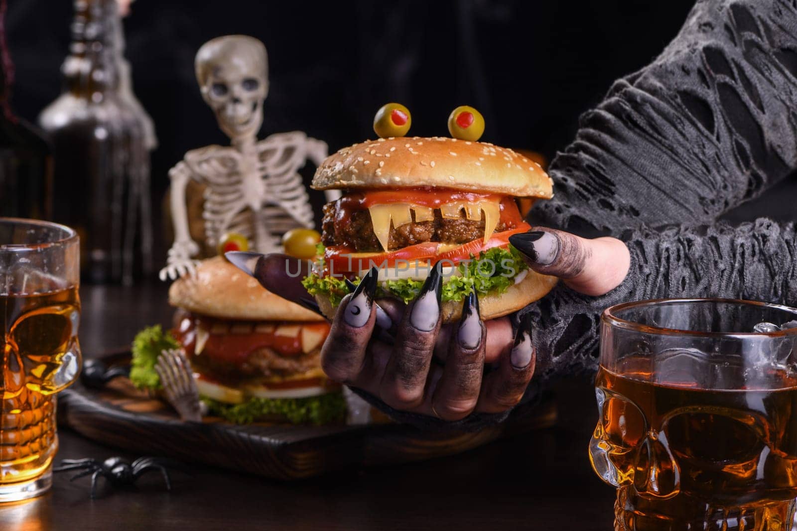 The witches hands hold a Monster Burger in her palms on a sitting skeleton. Perfect Halloween Party appetizer