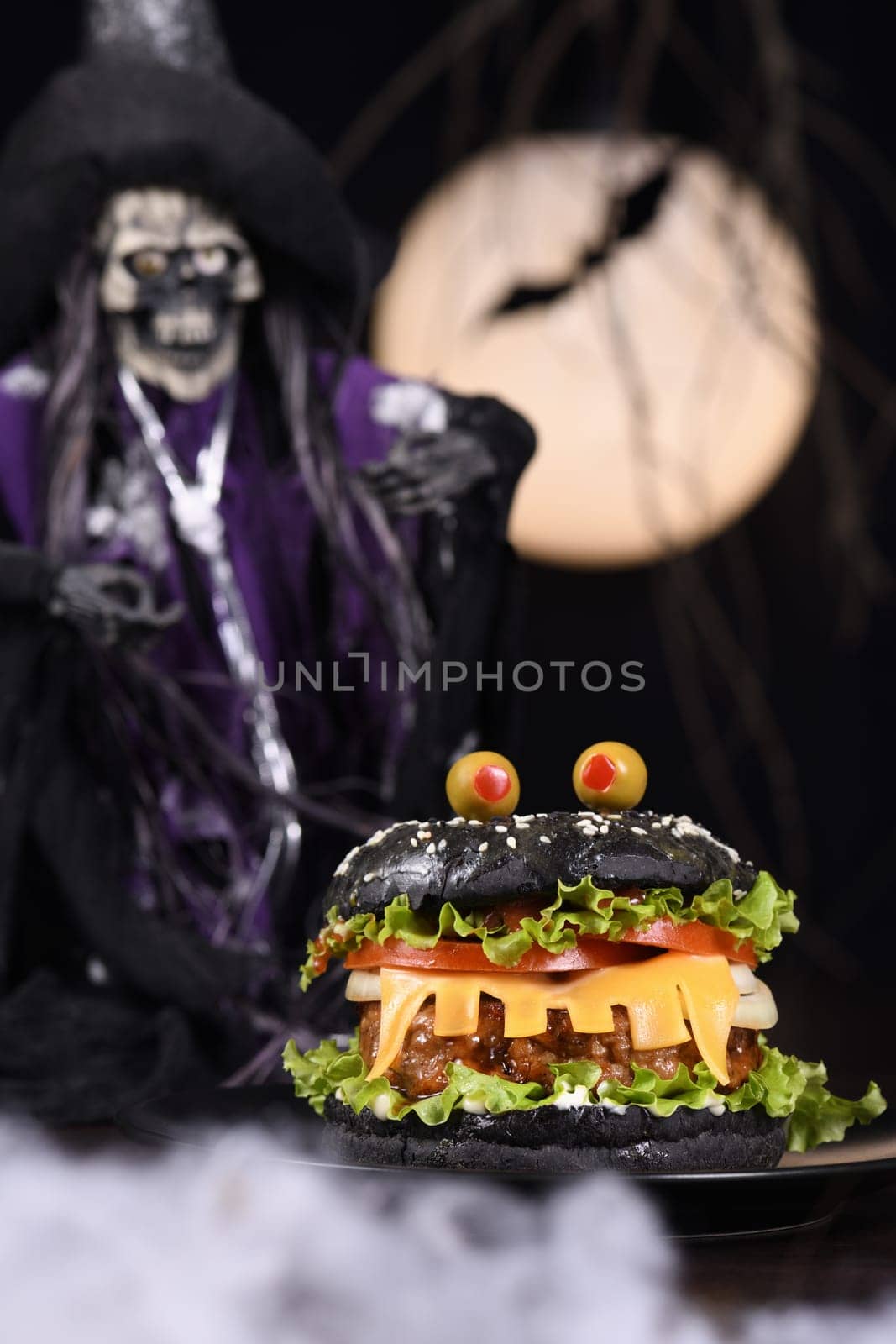 Monster Burger. Black bun, juicy beef cutlet, lettuce, onion, tomato and cheese in the shape of teeth, eyes with olives. Definitely a pick-me-up and a perfect Halloween party appetizer.