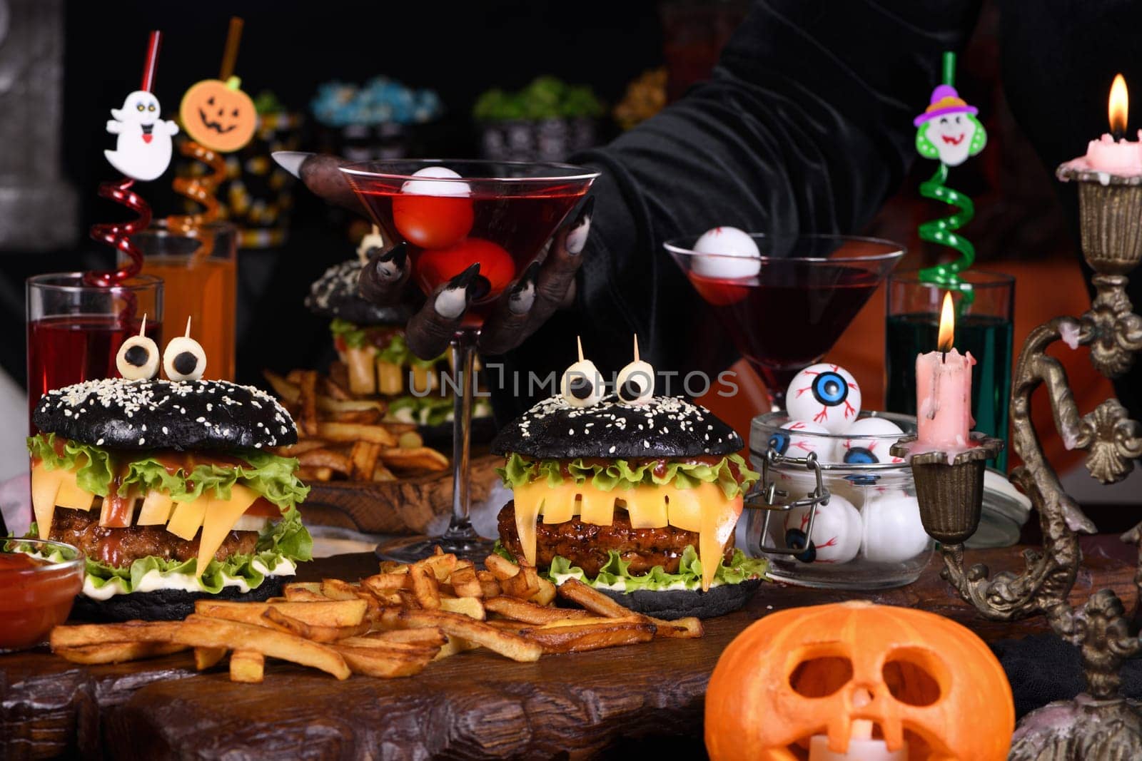 A witch's hand takes a Witch cocktail with eyeballs in a martini glass from the Halloween party table.