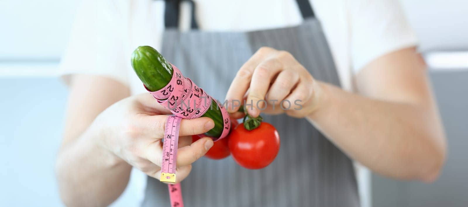 Close-up of person hold cucumber and tomatoes with measure tape around, create male organ with vegetables. Sport nutrition, health, fun, humour concept