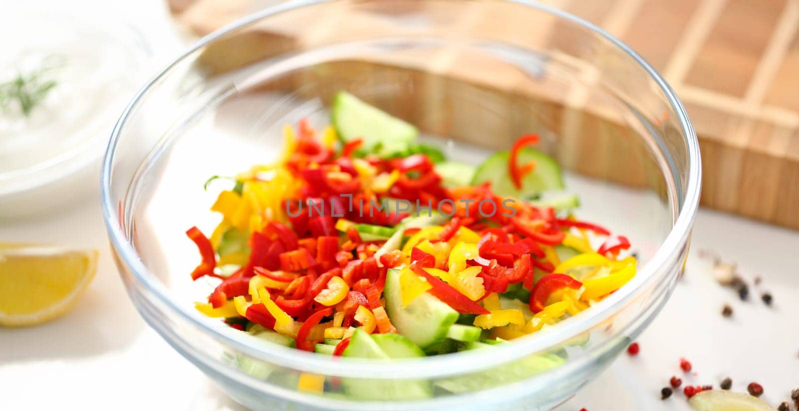 Close-up of delicious fresh salad with mellow vegetables, cucumber and pepper ingredients. Meal served in glass bowl. Cooking, organic, healthy concept