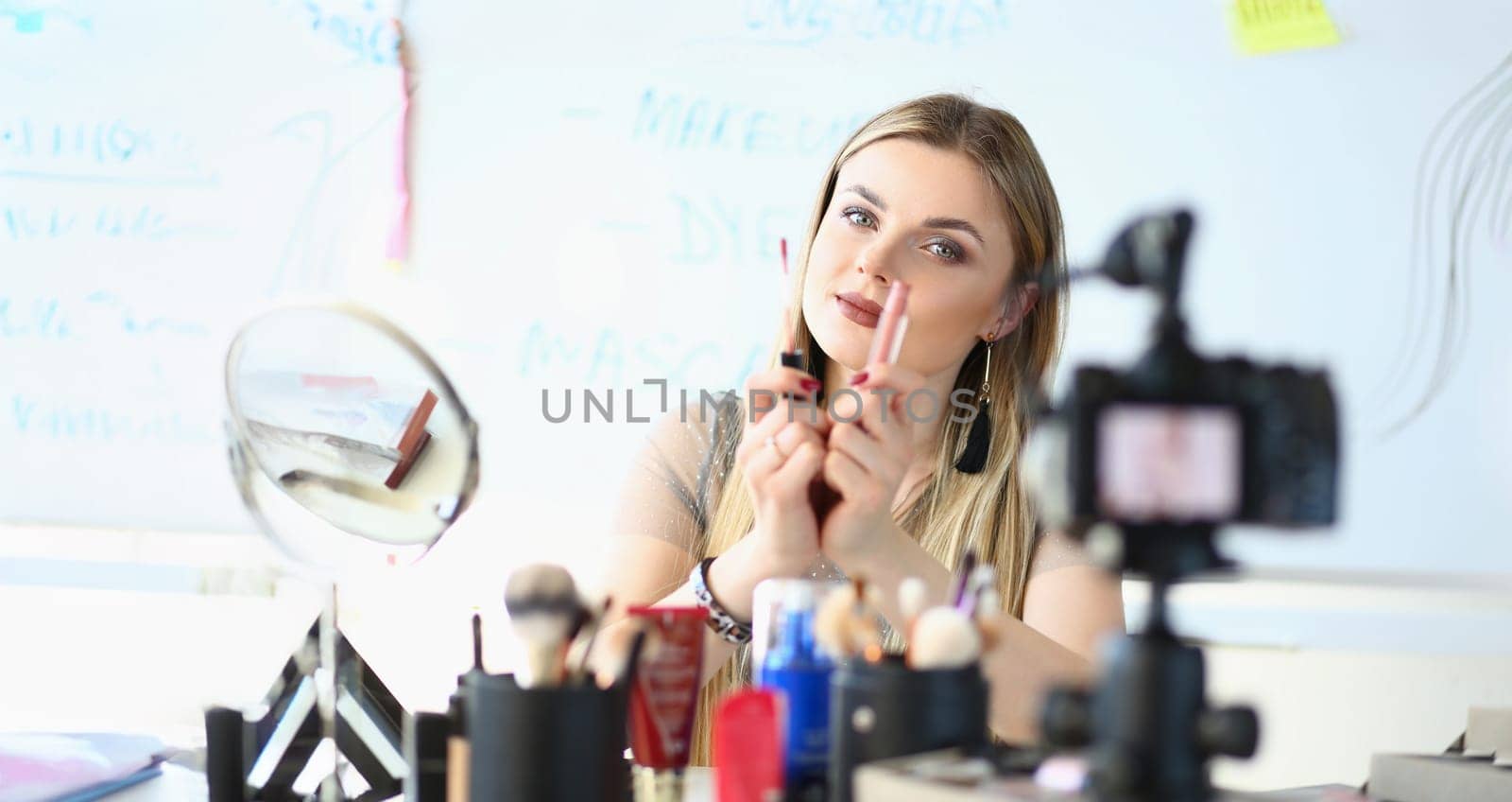 Portrait of pretty young woman wear makeup, glamour blonde woman visagist show lipstick on camera. Mua, beauty, art, hobby, social media content concept