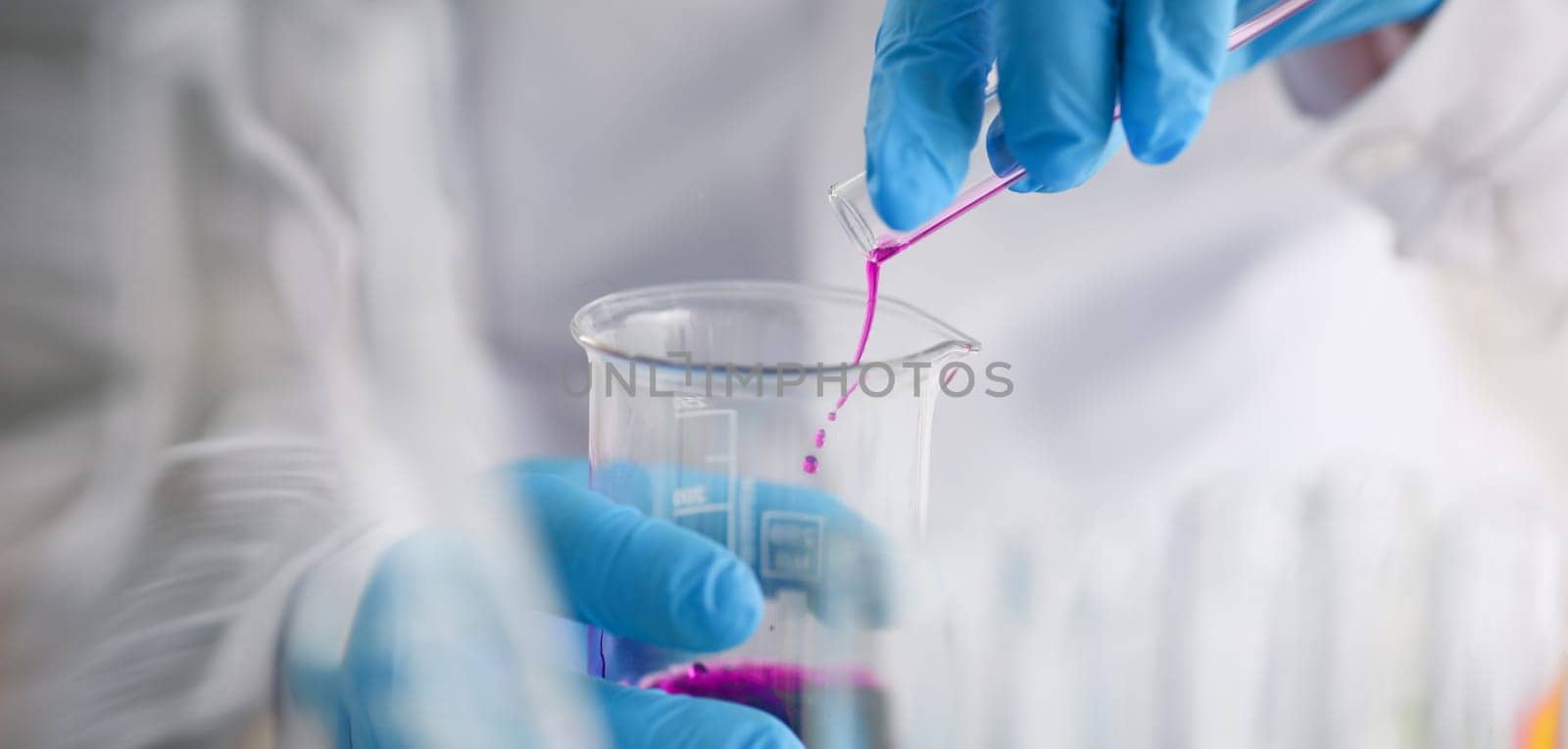 Close-up of scientist pour pink liquid from flask in medical chemistry laboratory. Chemist experiment with formula. Science, discovery, testing concept