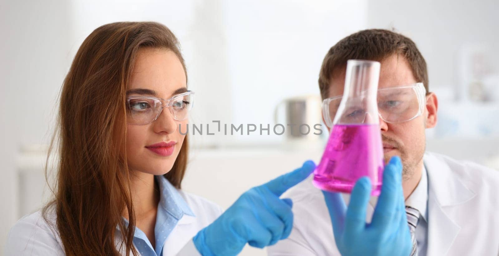 Portrait of smart scientists perform experiment in laboratory, bright pink liquid in glass. Biologist female and male colleague. Science, discovery concept