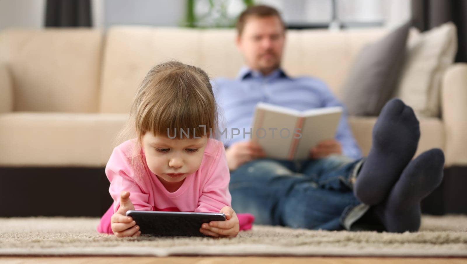 Portrait of little girl play with smartphone device, digital entertainment for kid, dad reading book. Childhood, parenthood, sparetime, addiction concept