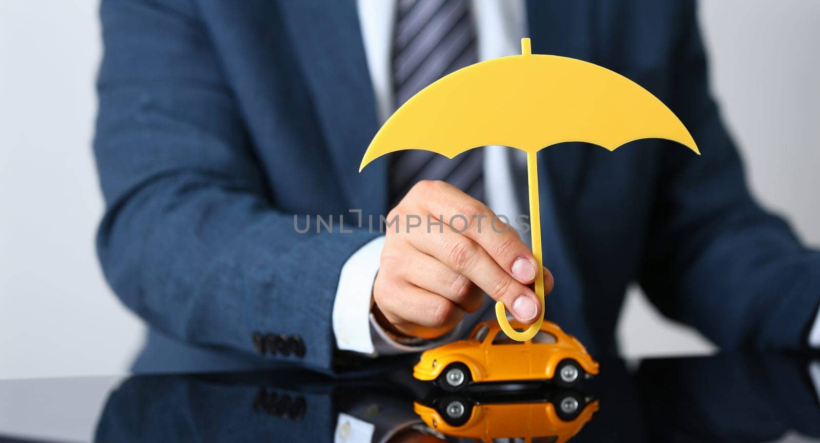 Close-up of man worker in suit hold wooden umbrella over yellow car model, symbol for car protection. Automobile insurance, safety, driver license concept