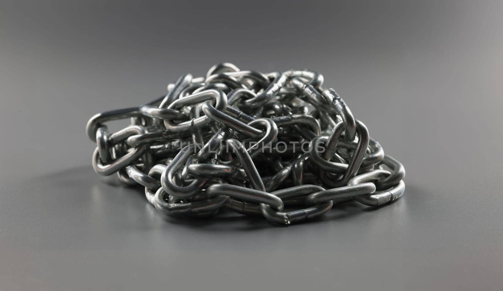 Close-up of grey chain folded in heap, steel metal iron chain on grey surface. Solid chain tangled in mess. Locking equipment, fixation instrument concept