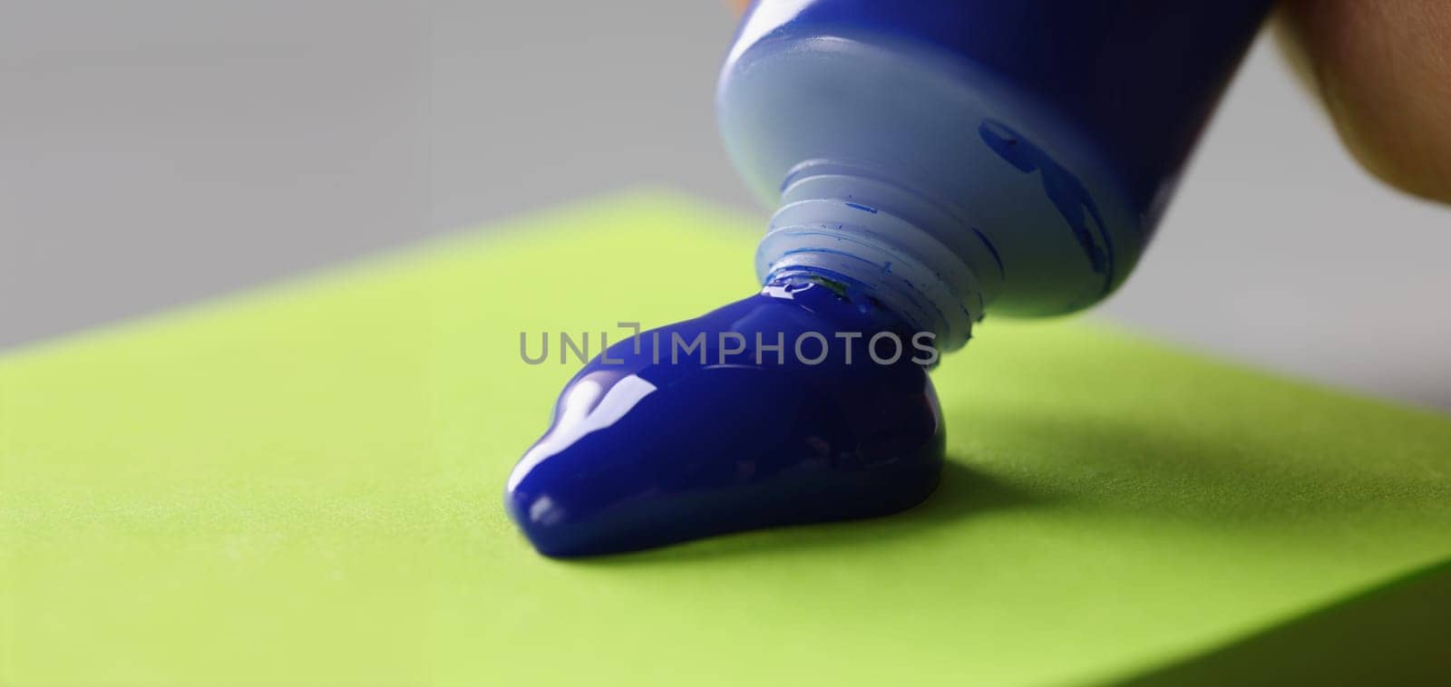 Close-up of man artist squeeze paint out of tube, bright blue colour on green paper. Tool for further creative masterpiece. Art, creativity, hobby concept