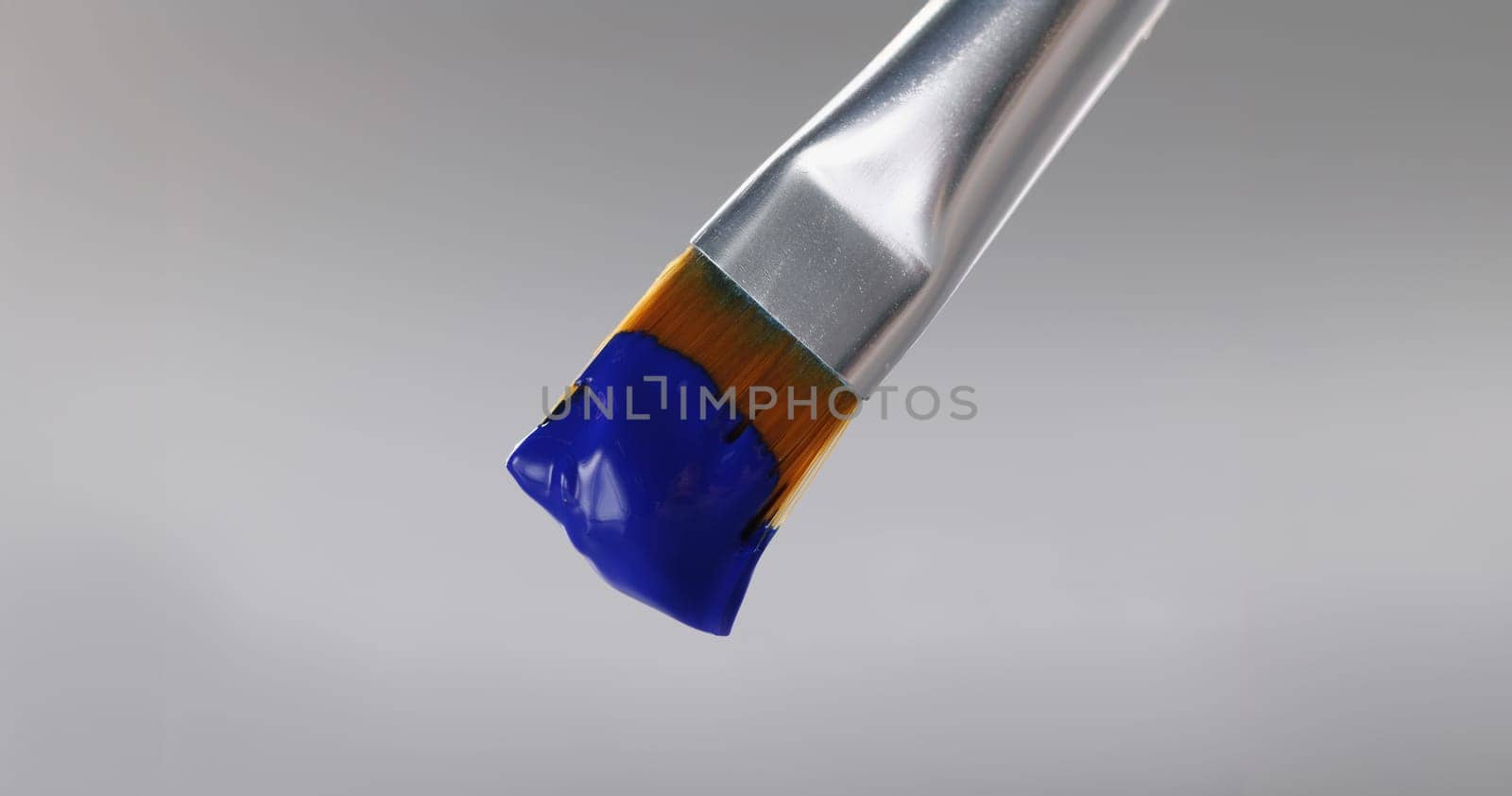 Close-up of brush with blue greasy oil paint on tip, professional equipment for drawing on grey background. Masterpiece, art, creativity, artistry concept