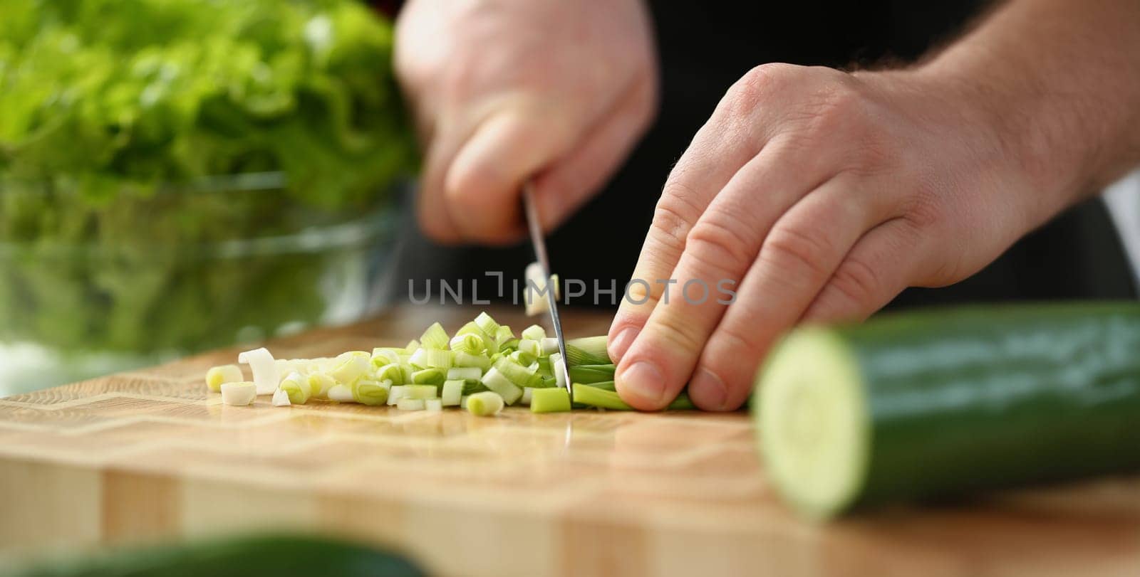 Close-up of professional chef cut spring onion with sharp knife on cutting board. Person follow delicious new recipe. Cooking, food, meal, homemade concept