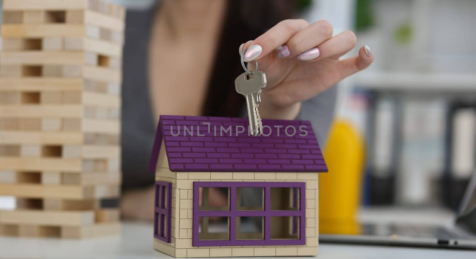Close-up of female worker hand hold key to unlock new miniature toy house, buy new accommodation, invest in real estate. Agency, mortgage, realtor concept