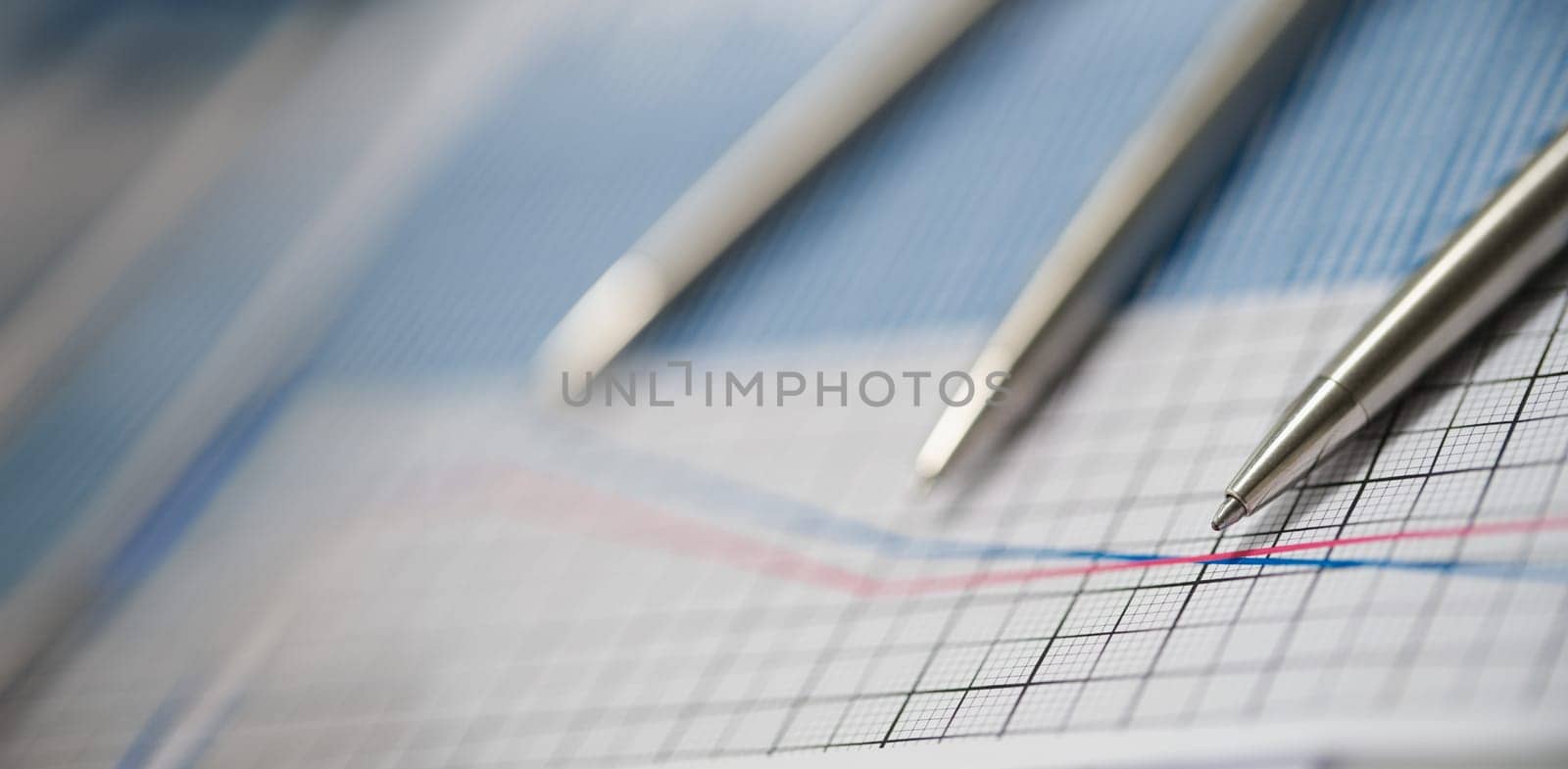 Close-up of business paper with graphic, blue and red line in increase and decrease order. Set of silver pens on top. Statistics, business, finance concept
