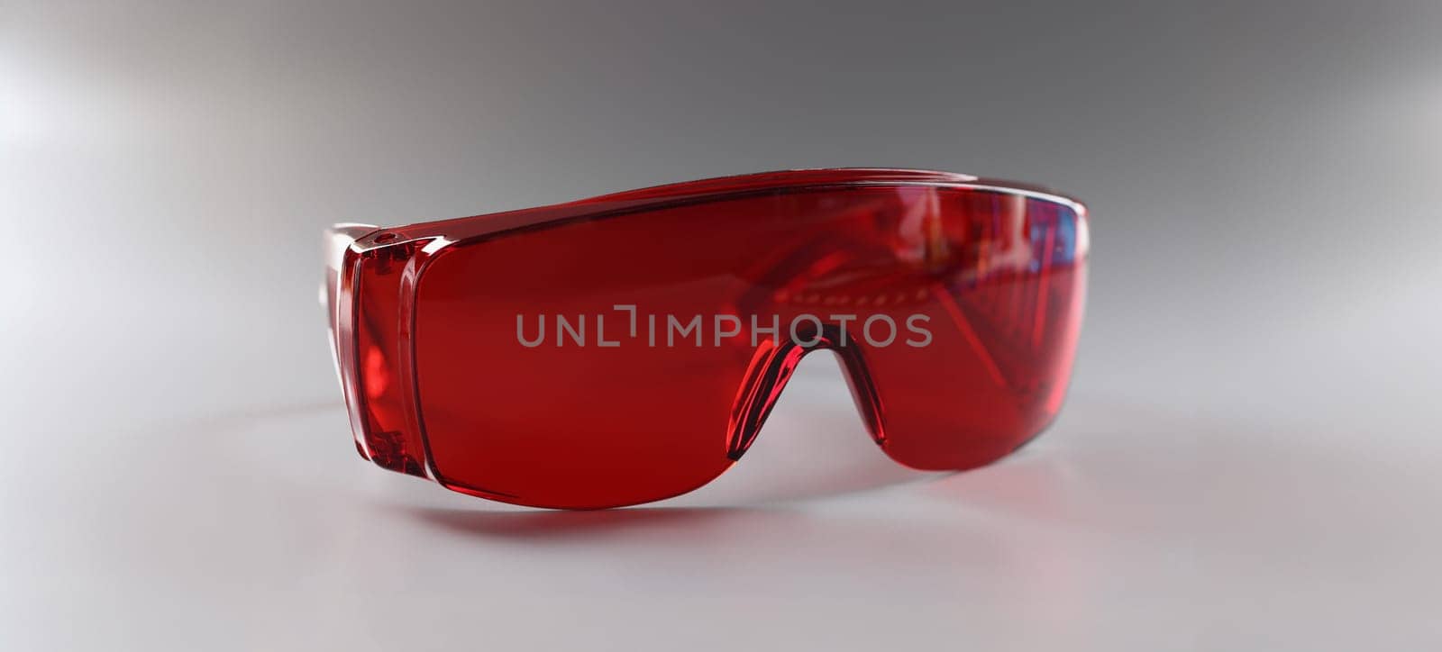 Close-up of red plastic safety glasses, protective workwear for human eyes. Reusable eyewear on grey surface. Occupational safety and eye health concept