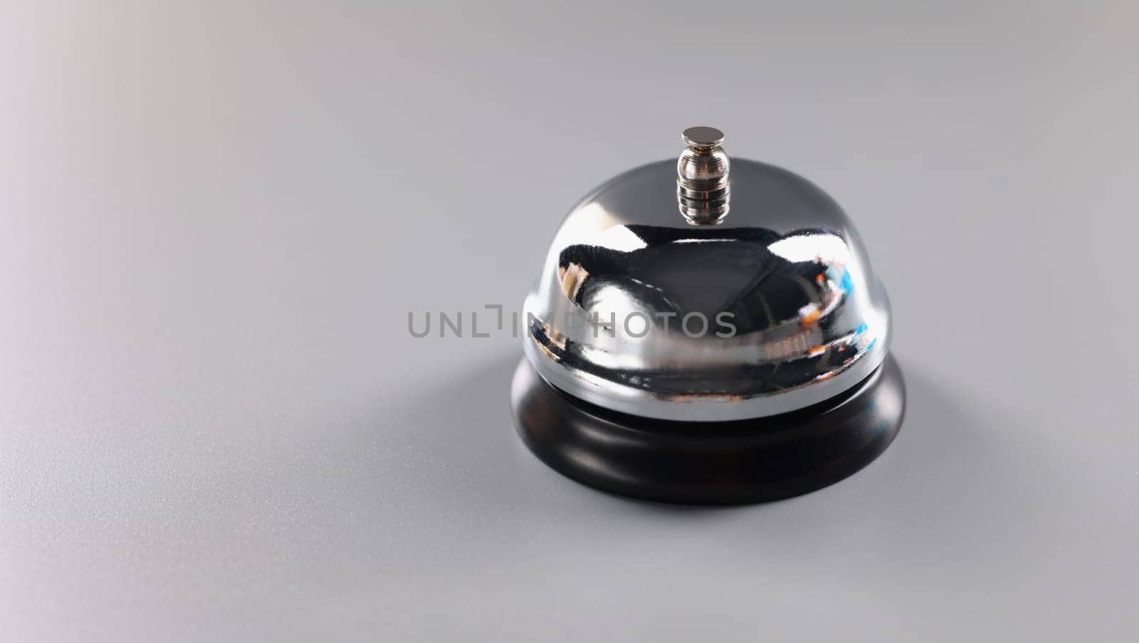 Close-up of silver bell stands on grey surface to attract attention, press bell to call service. Thing to put on reception. High quality service concept