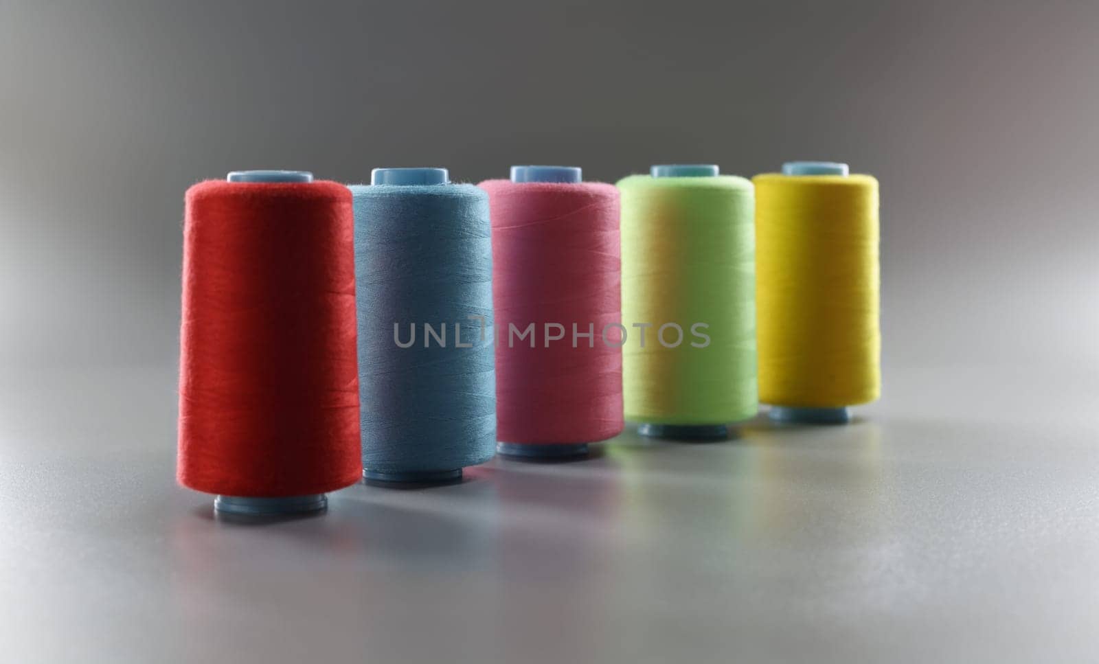 Close-up of group of whole haberdashery item colorful thread spools on grey surface. Colorful bobbins for tailoring. Dressmaking, atelier, fashion concept
