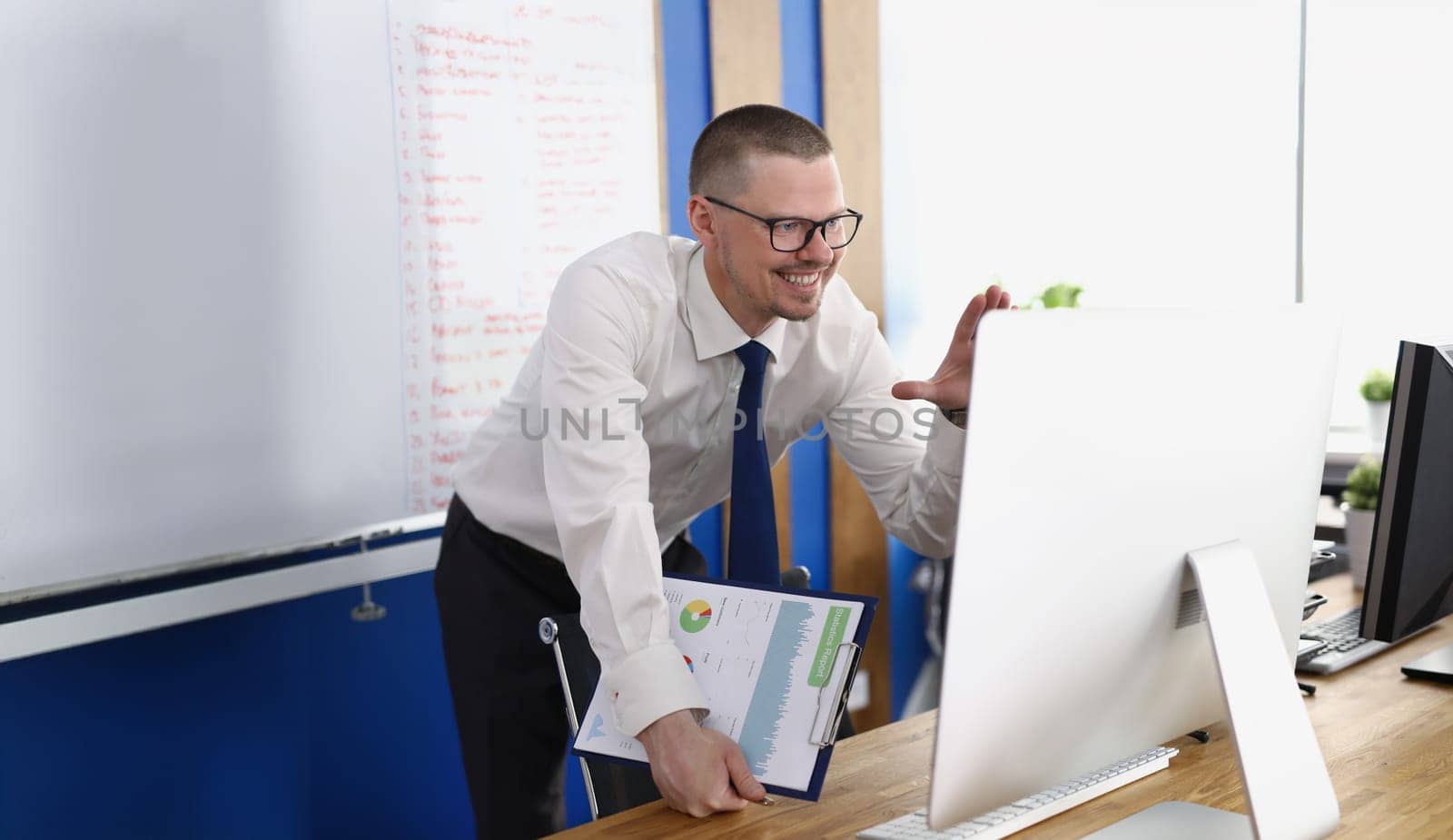 Portrait of smiling worker wave hi to online colleagues on video call. Computer on desk, board with lettering on wall. Business, conference meeting concept