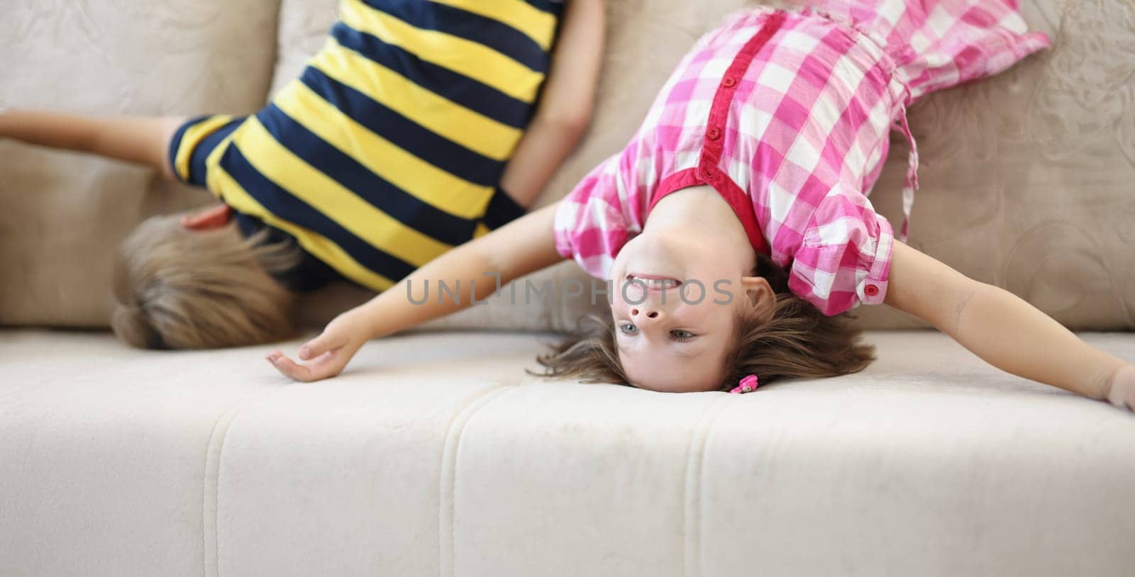 Portrait of children have fun at home, kids upside down on sofa, holiday at school. Sisters and brother made up fun game. Childhood, party, go nuts concept