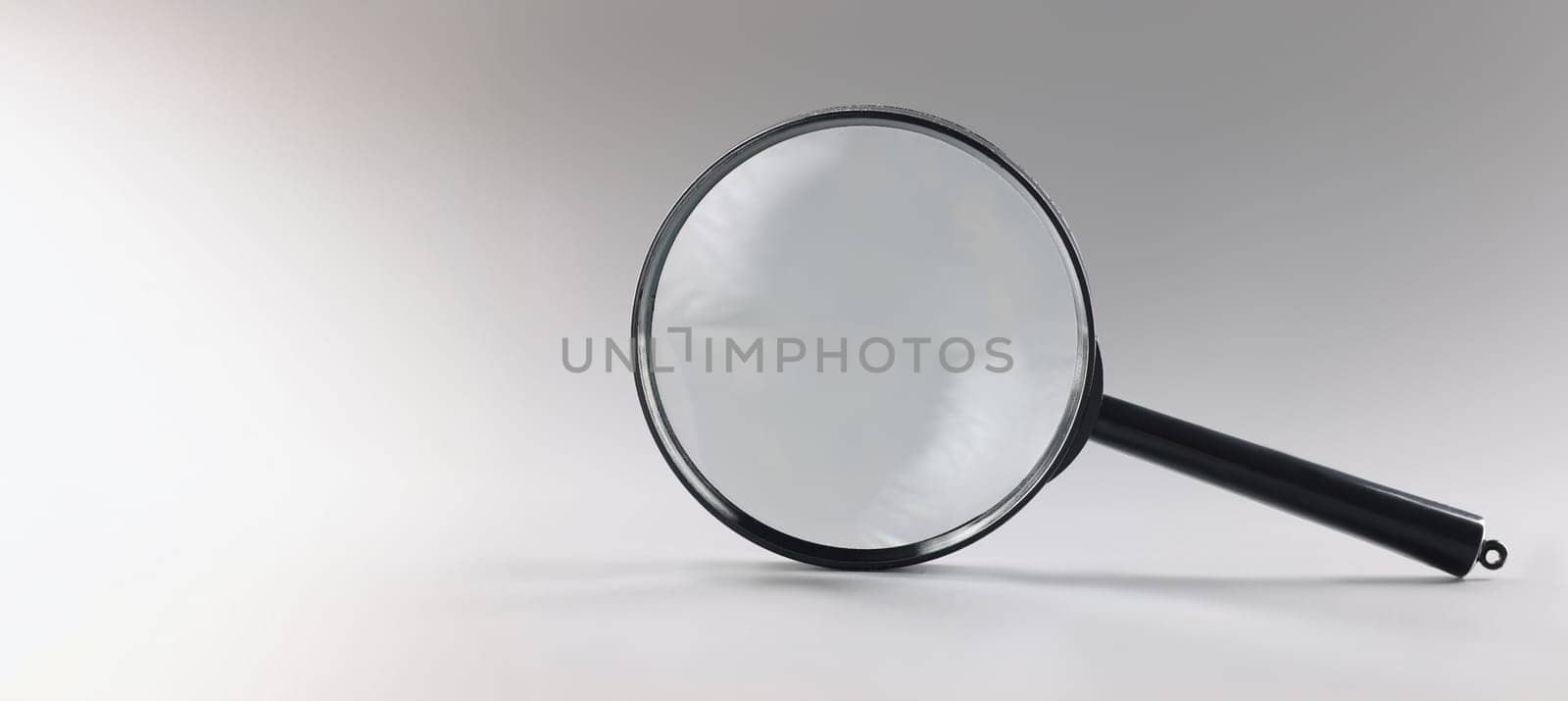 Close-up of single magnifying glass with black handle, leaning on grey surface. Simple design of lens or loupe to enlarge objects. Magnifying lens concept