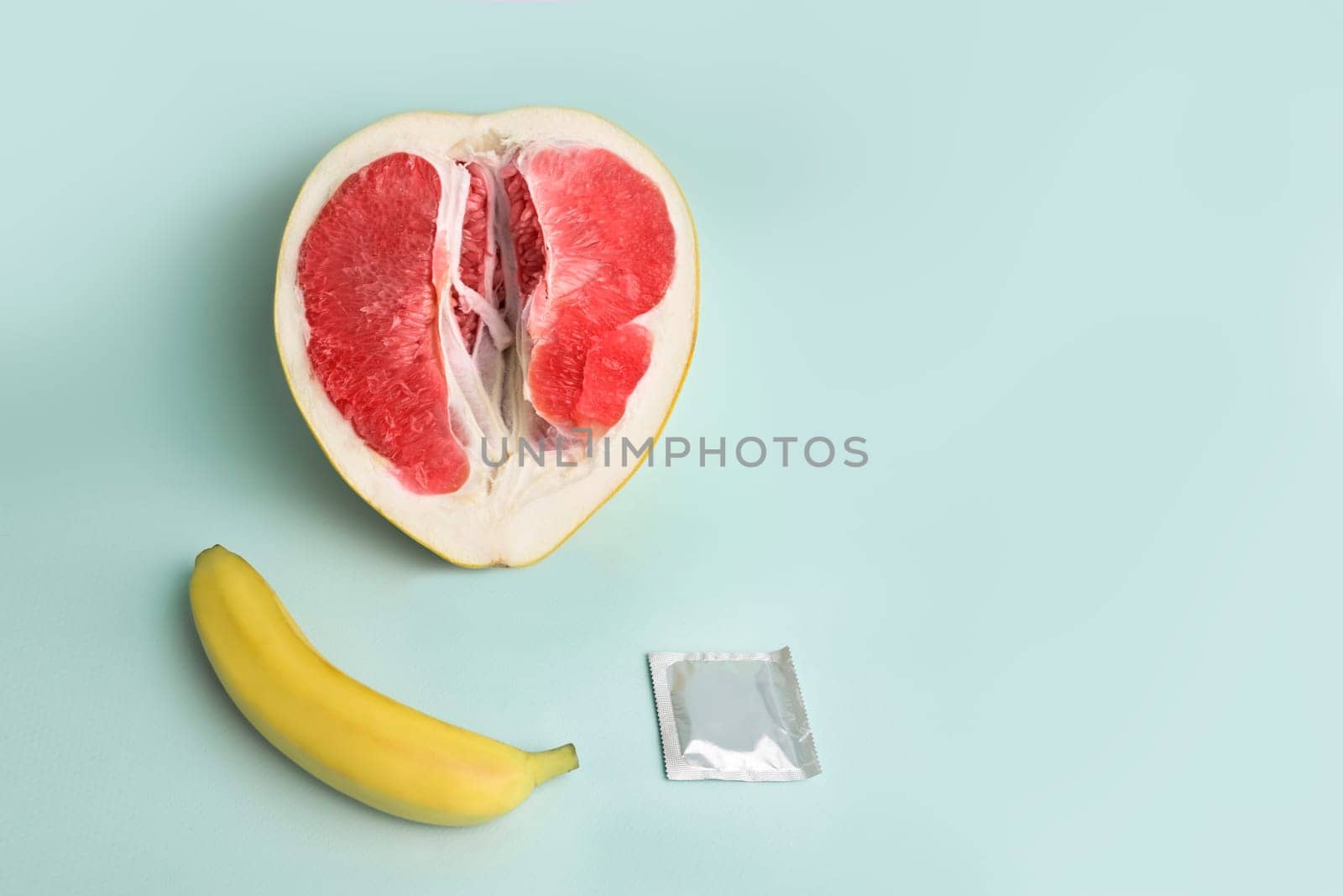 Safe sex. Juicy grapefruit and banana in a condom. The symbol of the vagina and penis from fruit.