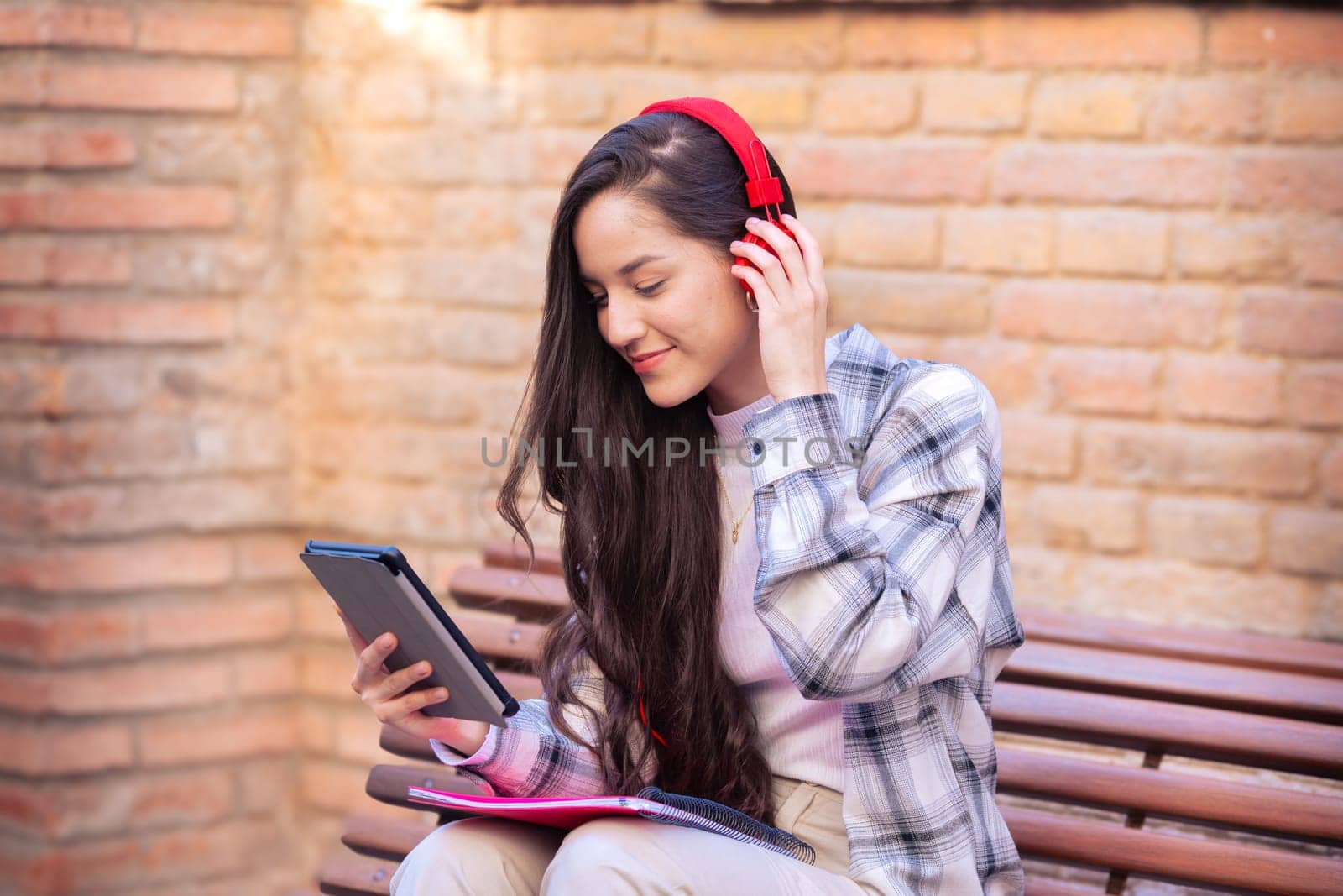 Young smiling student with notebook in hand uses social networks with tablet applications and wireless technology outdoors.
