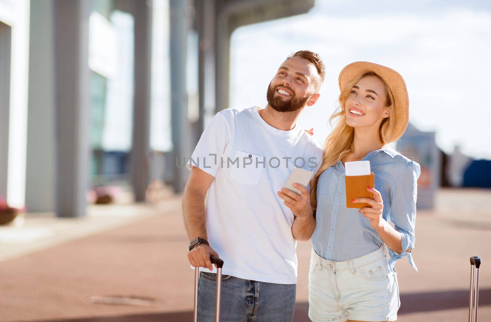 Traveling Concept. Smiling spouses looking up at plane, standing near airport terminal, blurred background