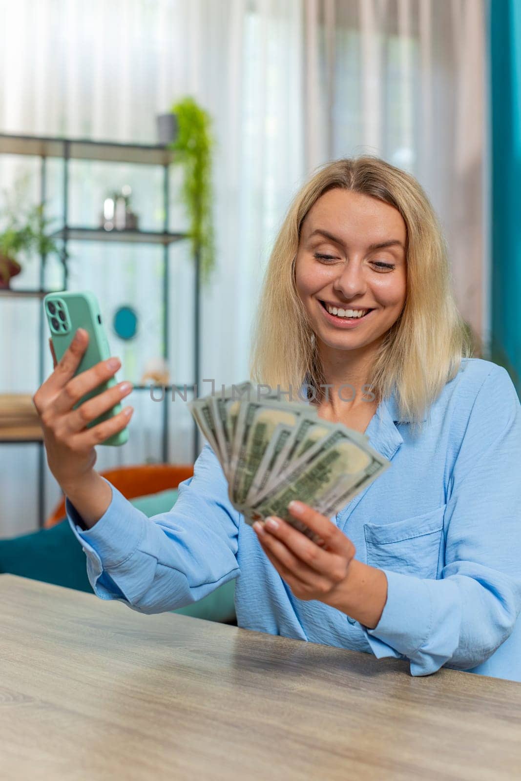 Happy rich businesswoman counting money dollar cash, using smartphone calculator app at home office workplace. Professional freelancer Caucasian woman rejoicing win, success contract, earning profit.