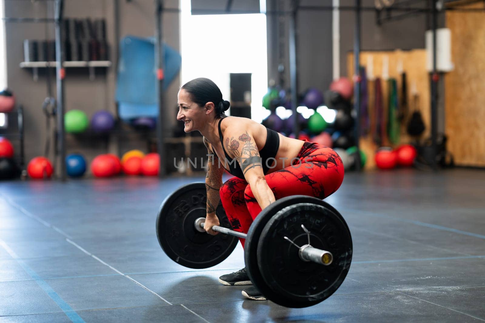 Mature sportive woman in squat position to lift weight in a gym