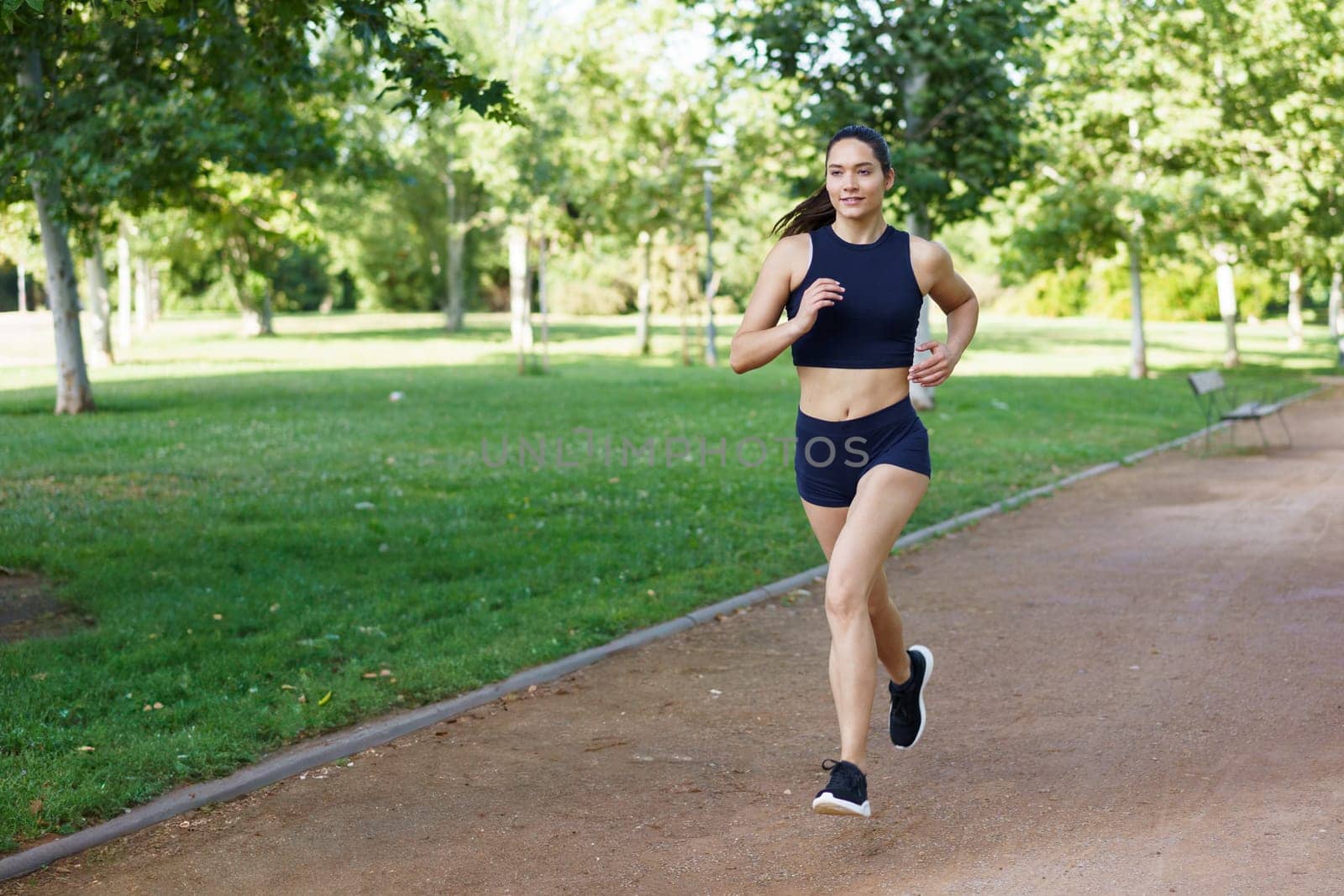 A young woman runs in a green park, embracing fitness and health. Ideal for conveying themes like lifestyle, exercise, and wellness. Keywords active, health, fitness, outdoors, wellbeing