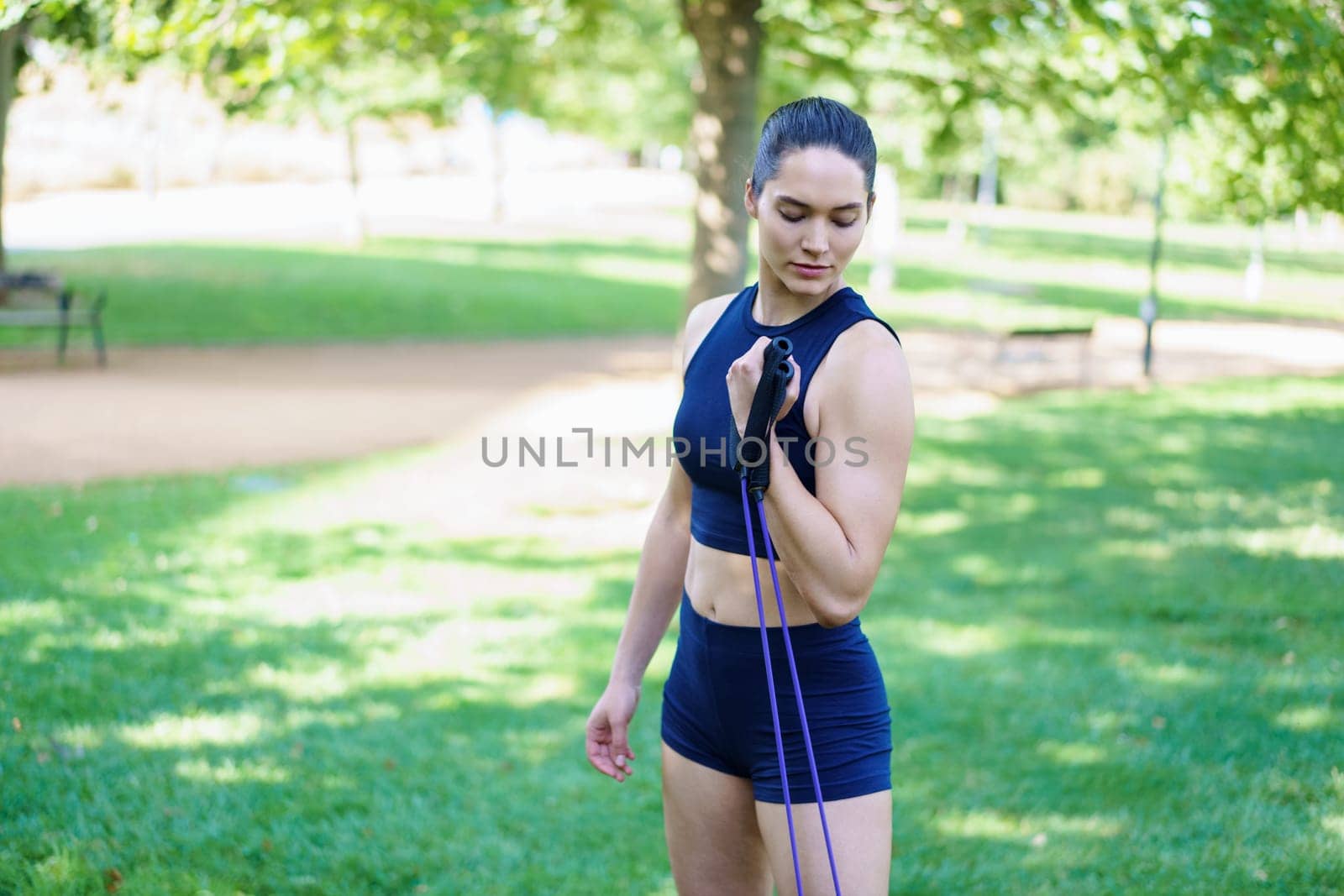 Athletic woman in sportswear exercising with resistance bands in a scenic park setting, showcasing strength and fitness