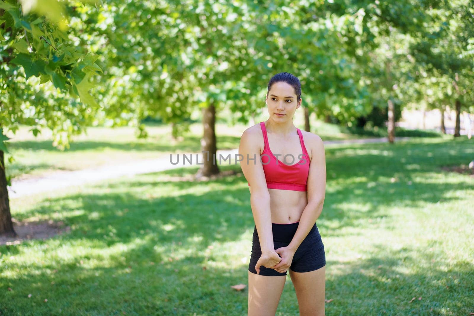 In a lush green park, a determined young woman in pink sports bra and black shorts is deeply focused on her exercise routine, displaying energy and dedication amidst natures beauty