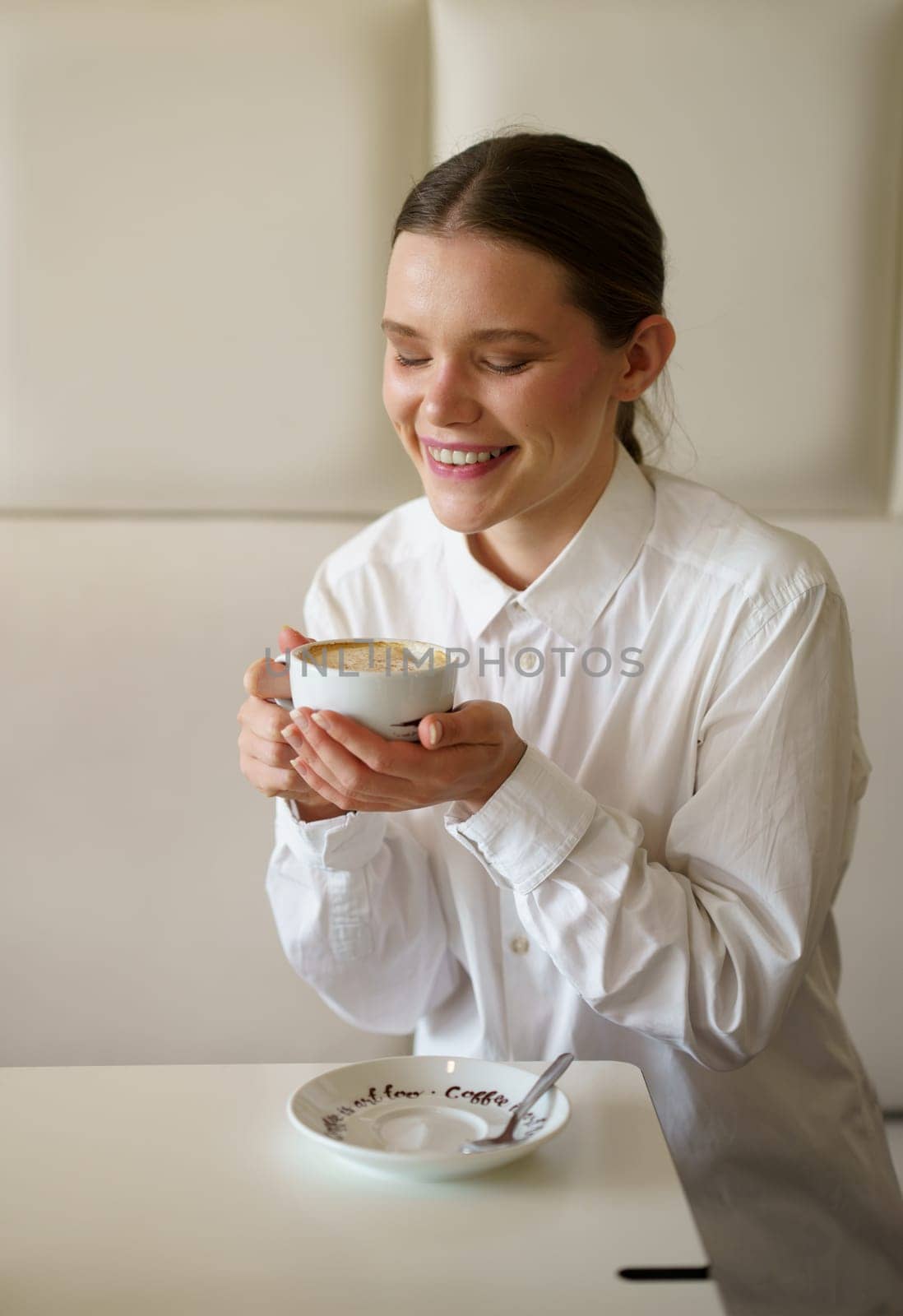 Vertical photo of a caucasian smiling businesswoman enjoying morning coffee alone in a chic cafeteria