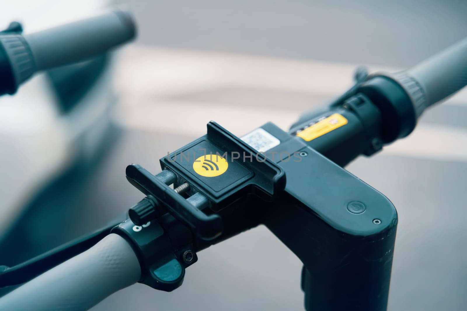 A closeup of a phone holder mounted on a scooters handlebar, showcasing a practical and convenient bicycle part. This useful tool is perfect for securely holding your phone while on the go