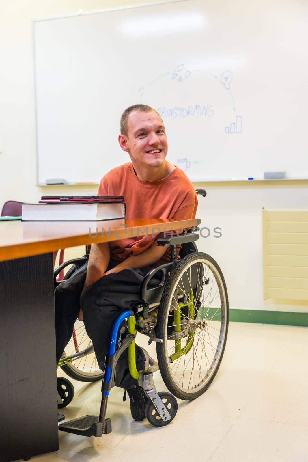 Vertical photo of a man with disability in a wheelchair in the university using tablet to study
