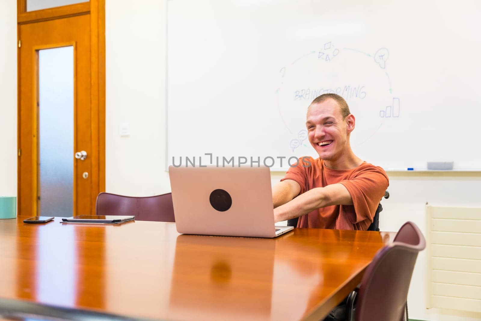 Smiling caucsian man with cerebral palsy working using laptop in a meeting room in a coworking