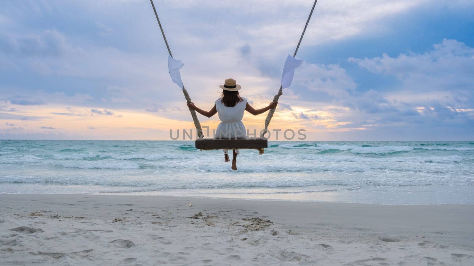 Asian Thai woman on a rope swing under a palm tree watching the sunset on the beach of Koh Kood Island Thailand