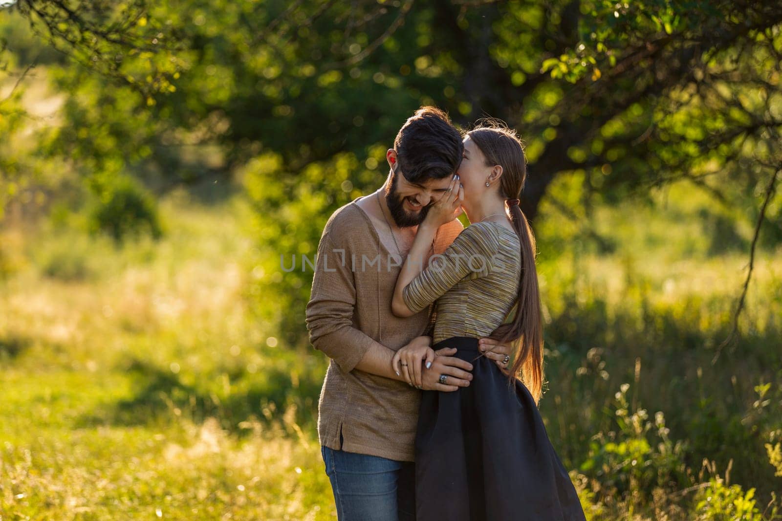 girl says something in the ear of her boyfriend, walking in nature