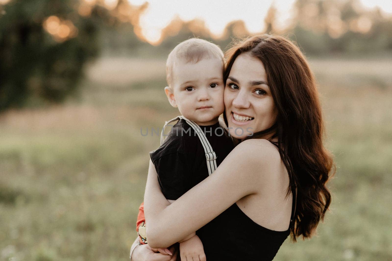 young Caucasian mother smiles hugging her little son in the summer. Added grain simulates film