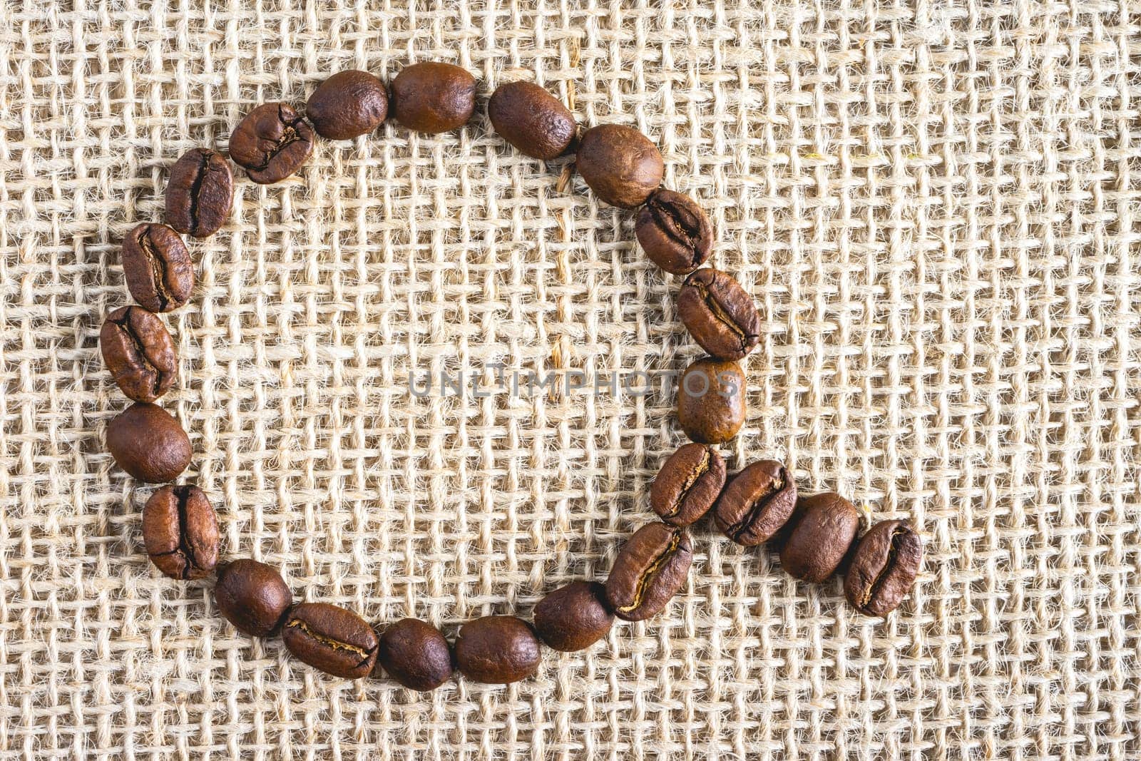 Coffee beans in the shape of a cup, on a burlap fabric. Background voor coffee related products.