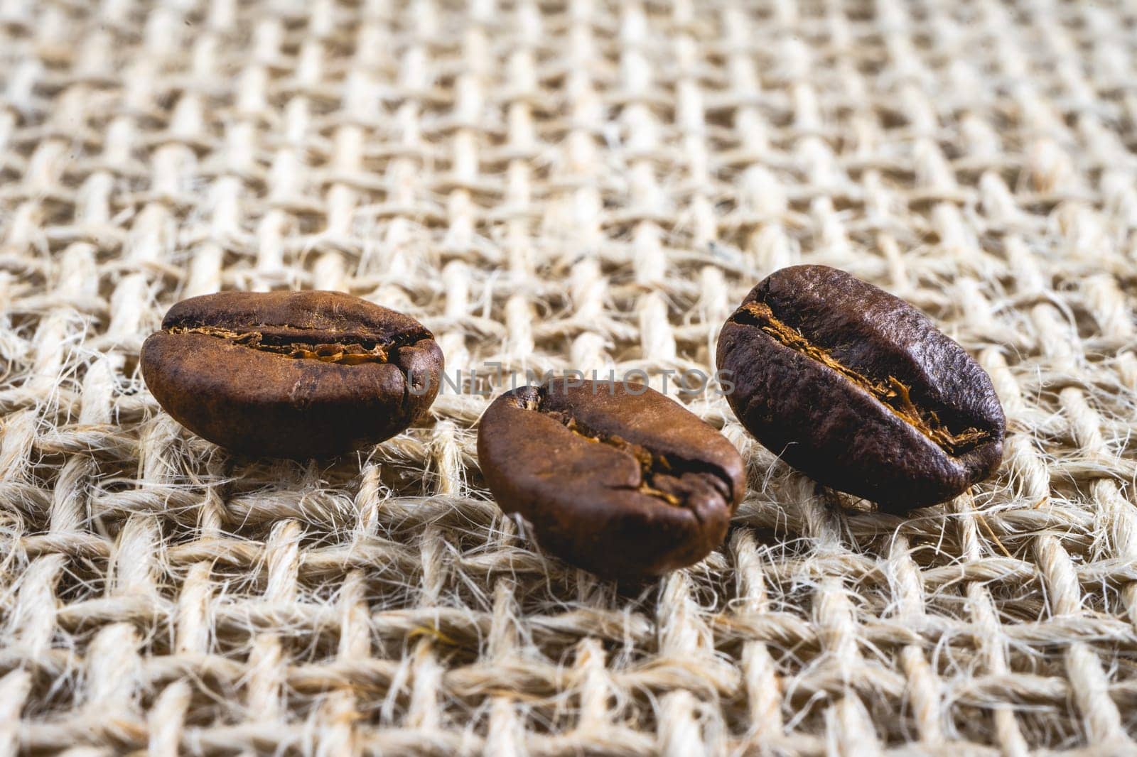 Close up from a few coffee beans laying down on a Burlap fabric background. Background voor coffee related products.