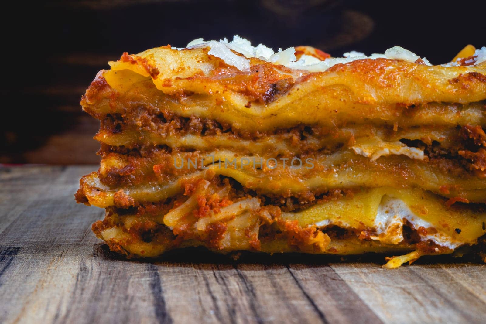 Close up view from a home made Lasagna, on a wooden table, and a dark background.