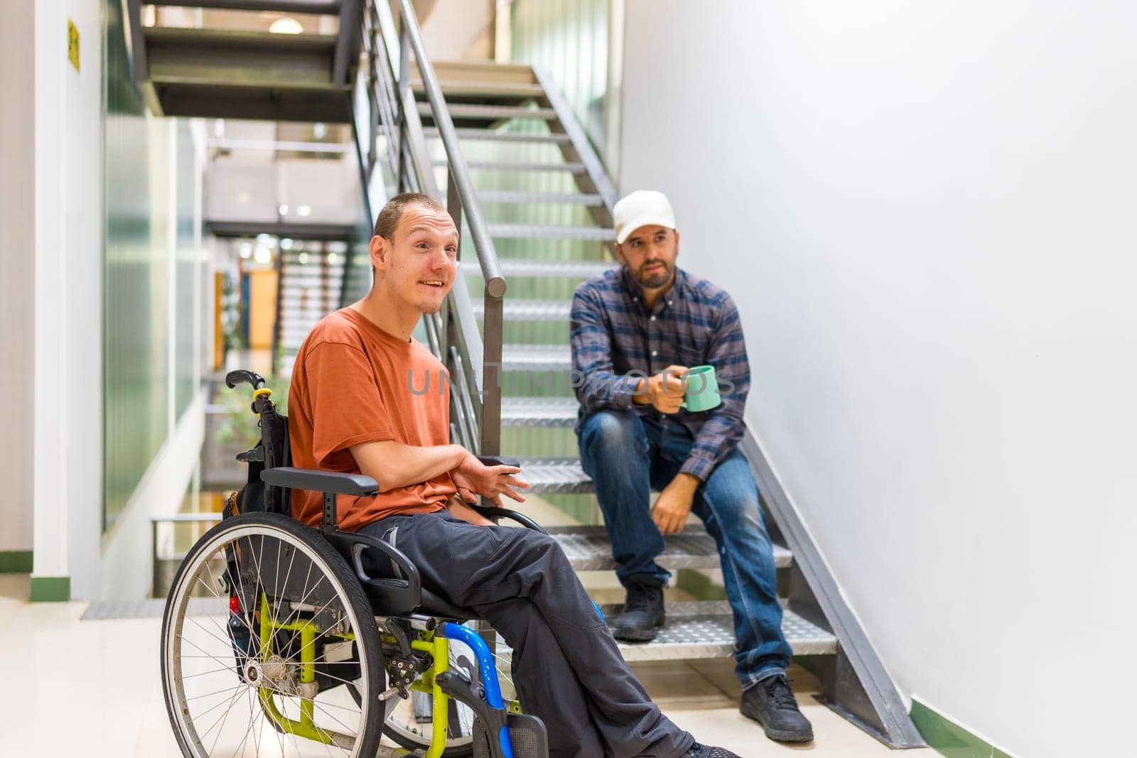 Man with cerebral palsy talking with a work colleague indoors in a modern coworking with staircase