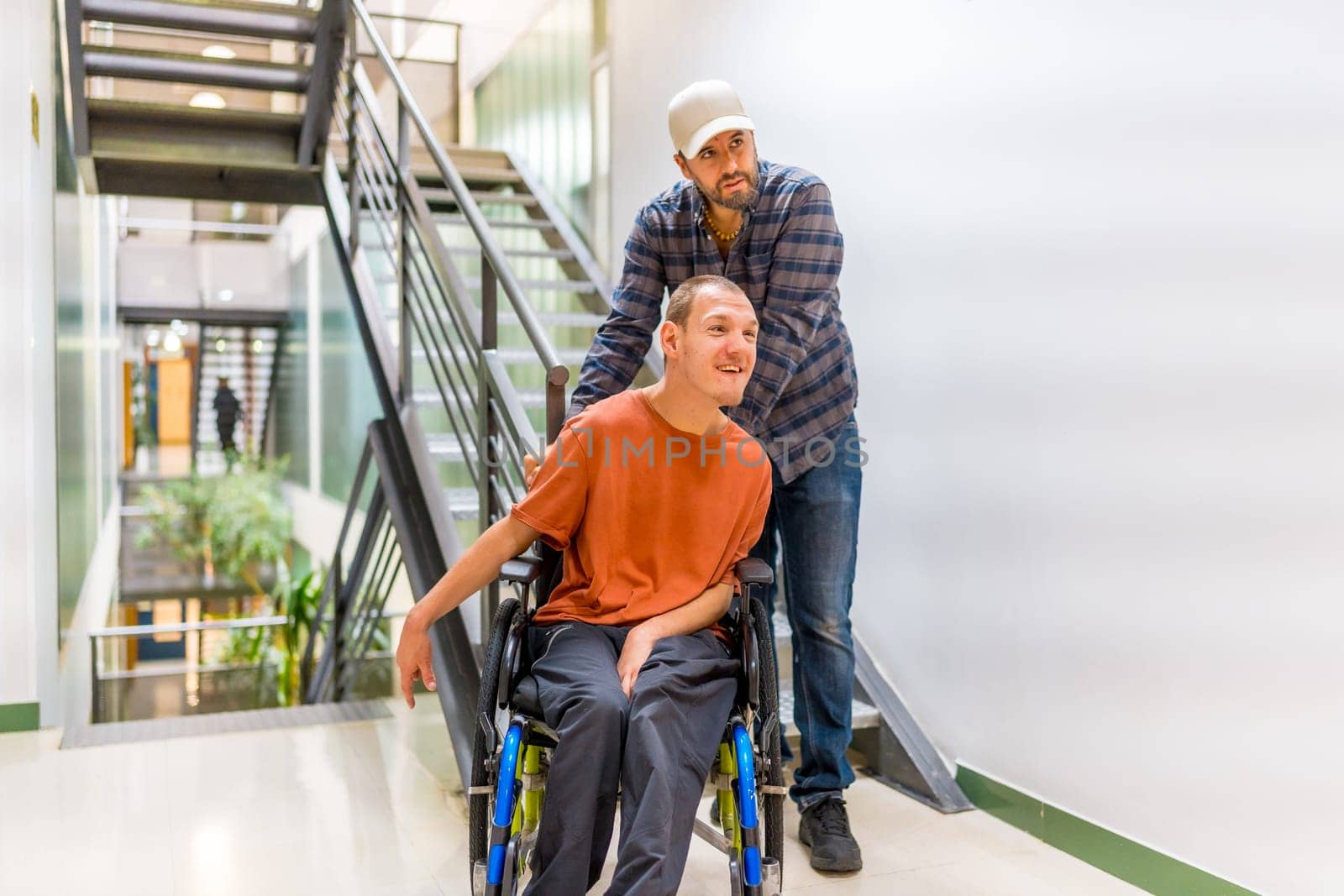 Man assisting a coworker with disability walking and pushing his wheelchair along a corridor