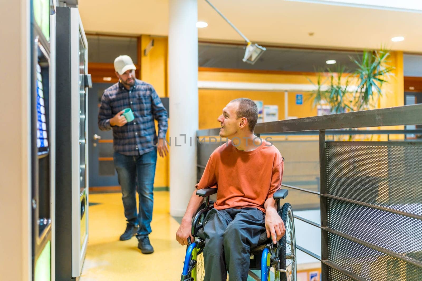 Coworkers walking into vending machines in a work break. One of them are a man with disability sitting on wheelchair