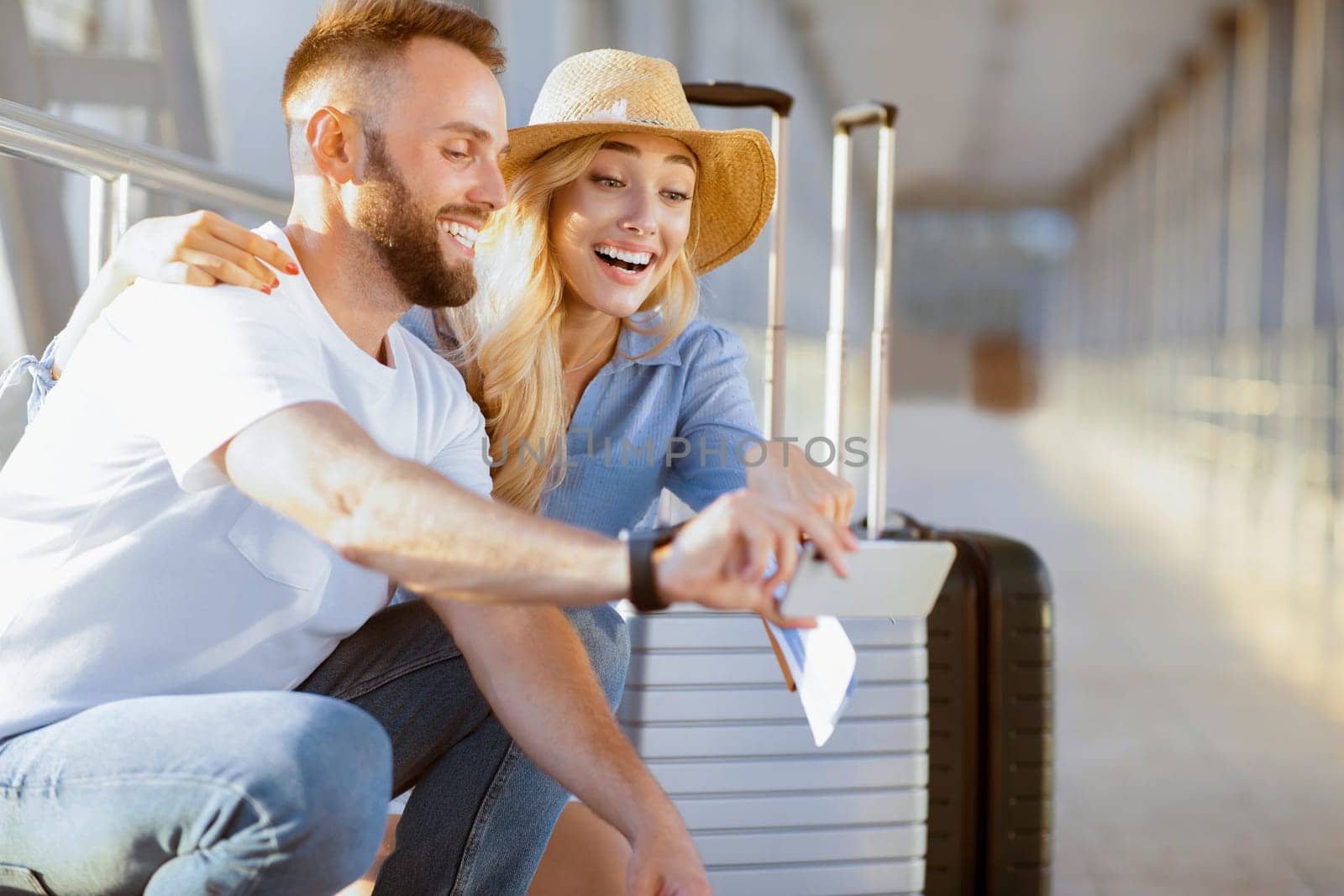 Excited couple in airport using smartphone, searching sightseeings, waiting for departure, free space