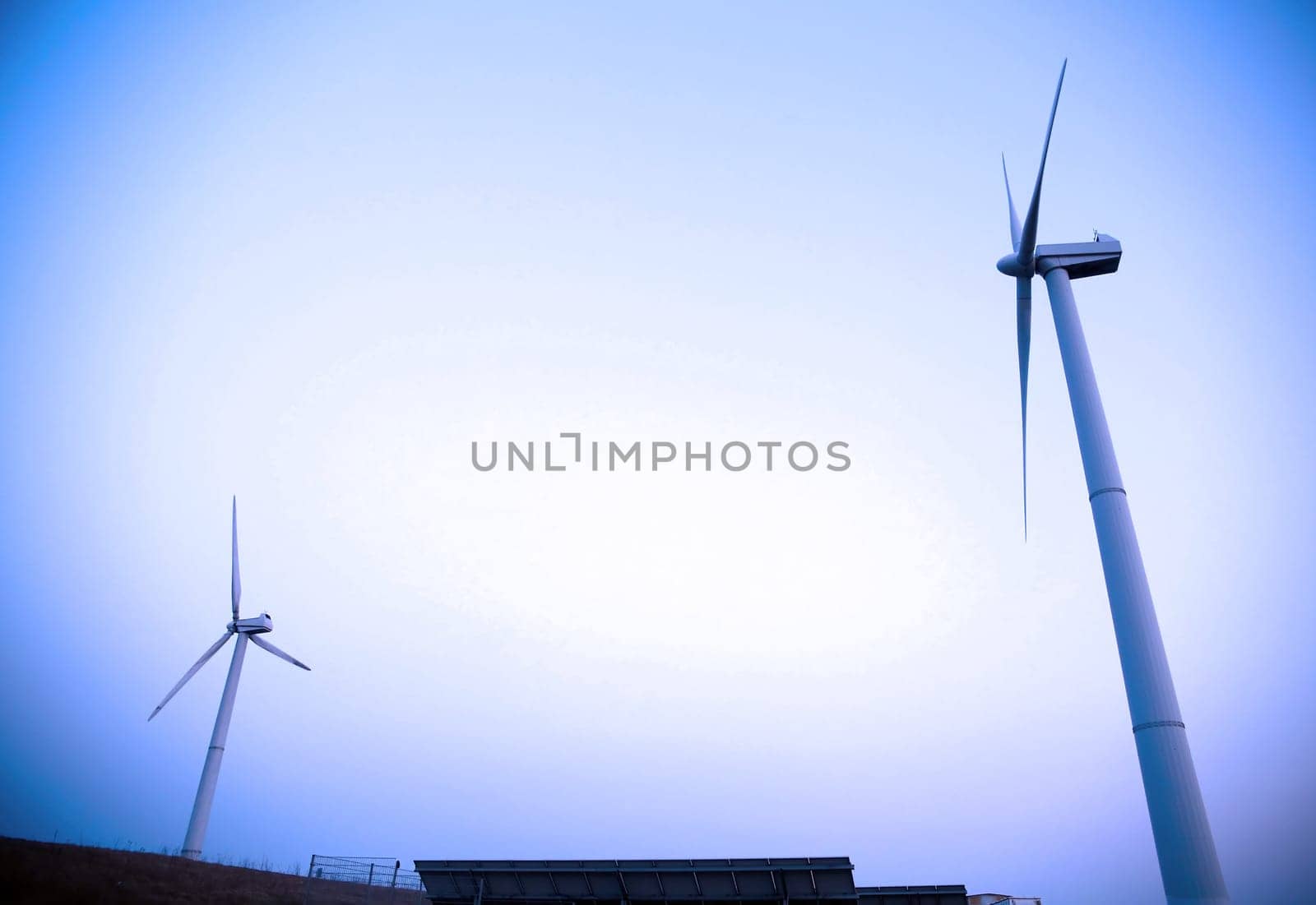 A cluster of wind turbines stand tall against a clear blue sky, their blades spinning energetically to harness wind power for energy generation.