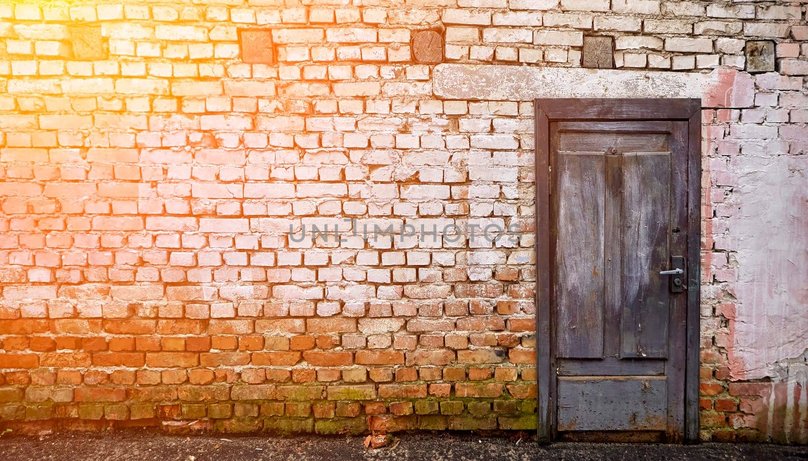 The vibrant blue wooden door, set against the weathered brick wall and adorned with remnants of whitewash, exudes a sense of history and charm, creating a timeless and welcoming atmosphere.