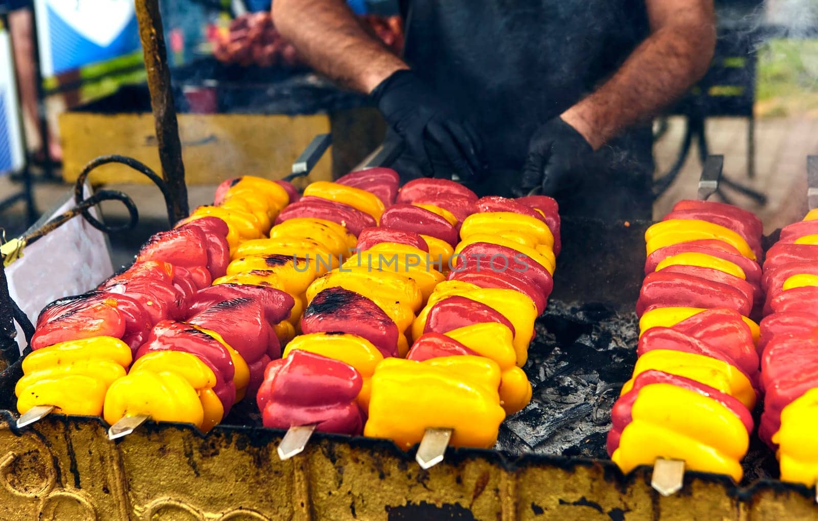 Colorful bell peppers on skewers grilling outdoors, sizzling and charred. A delicious smoky aroma fills the air, creating a vibrant and appetizing scene for a summer barbecue gathering.