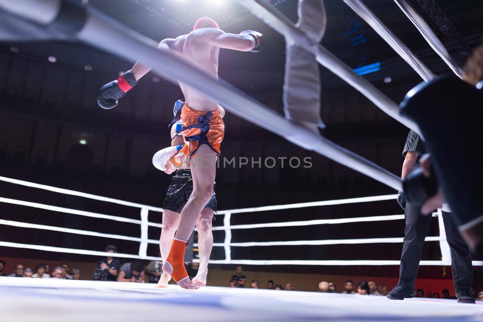 A man in a boxing ring is about to fall. The crowd is watching the match. Scene is intense and suspenseful