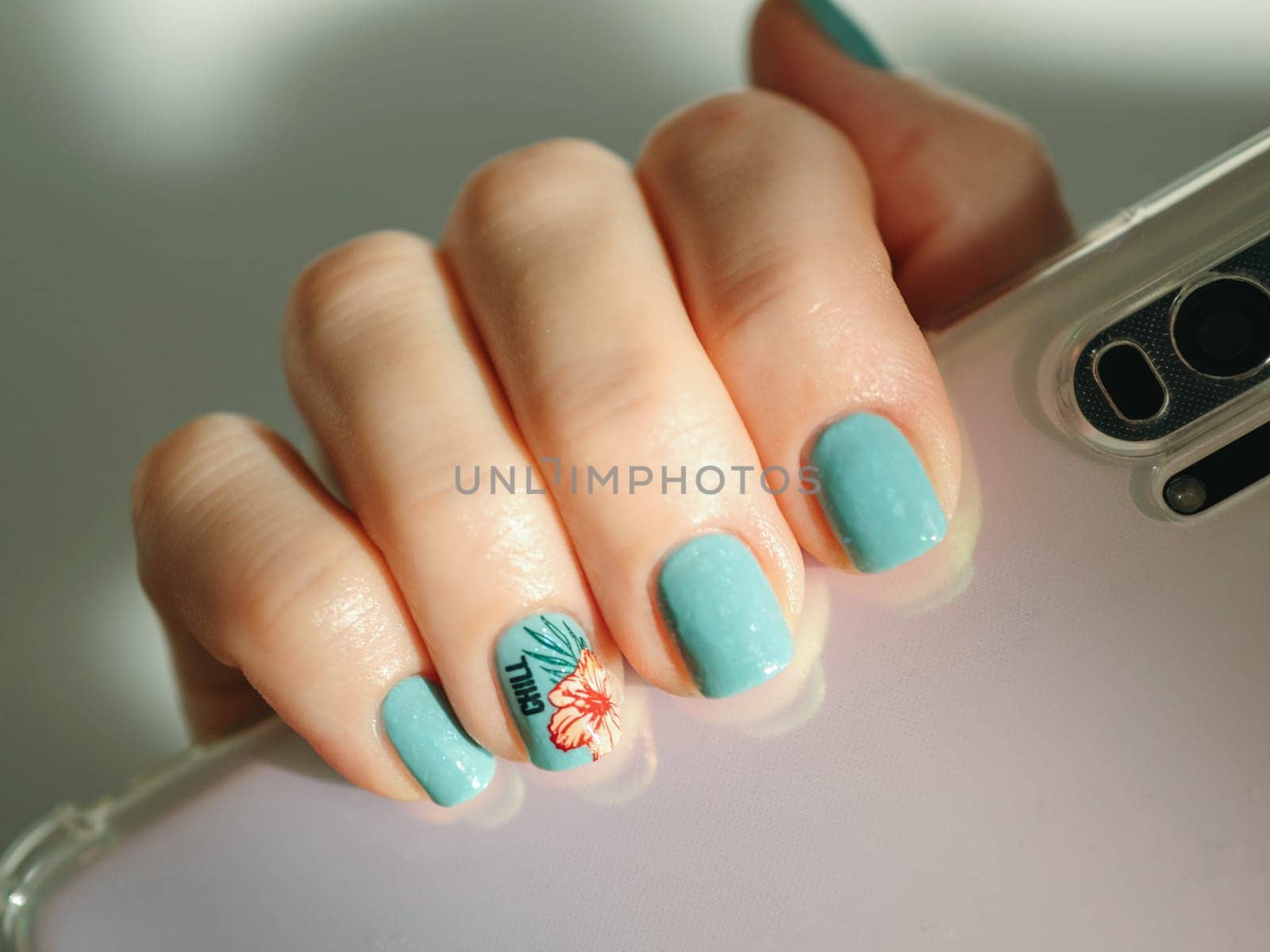 Aesthetic visual of fingernail with short nail with blue green manicure with reverse stamping summer tropical flower. Nail closeup with stylish pink flower in reverse stamping nail art design manicure