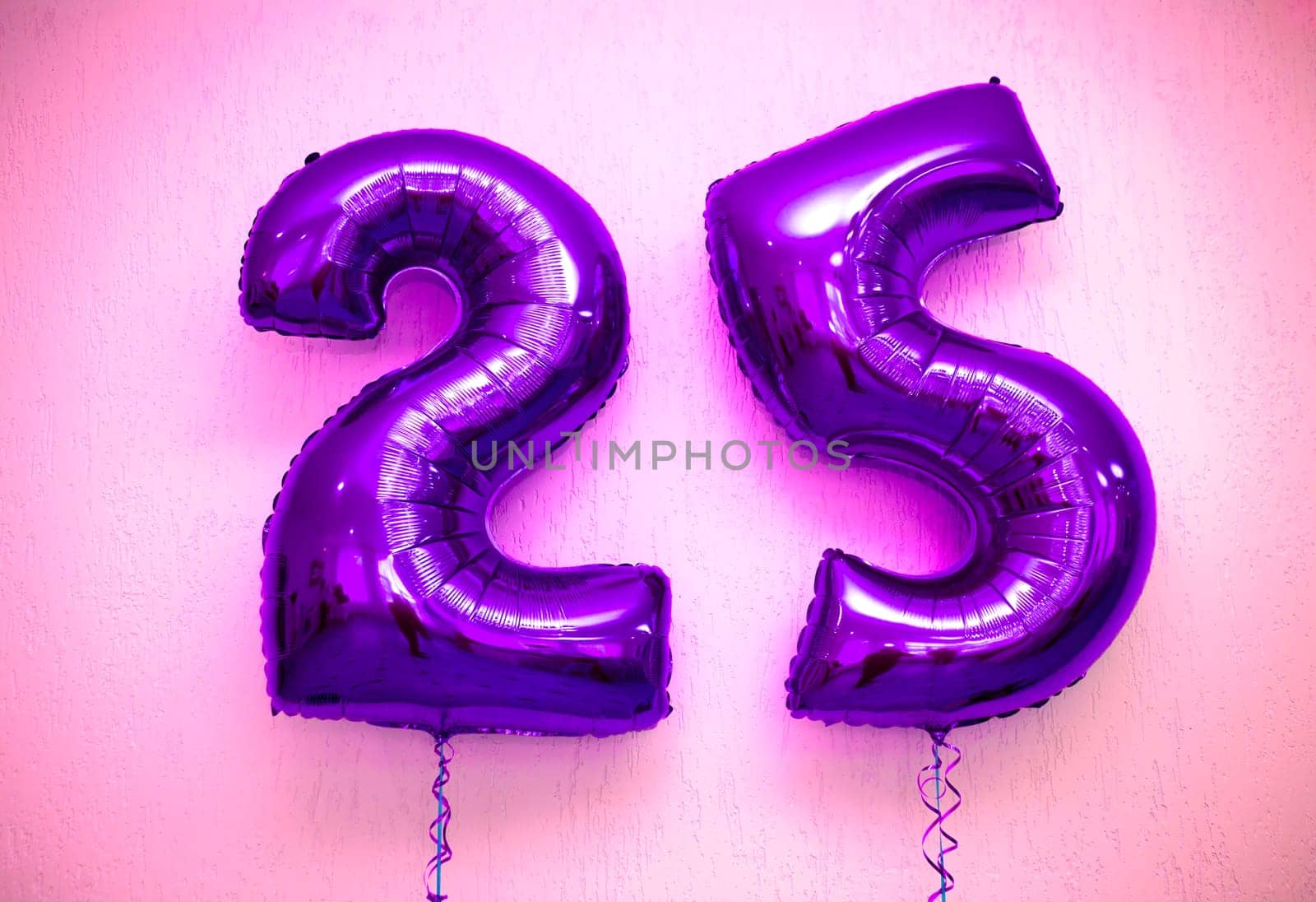 Two shiny purple foil number balloons, 2 and 5, floating gracefully against a soft pink background. The vibrant colors and elegant design make it perfect for various celebrations and events.